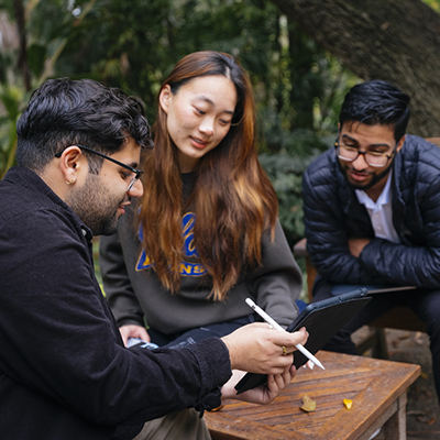 Three people looking at a tablet at a table outside.