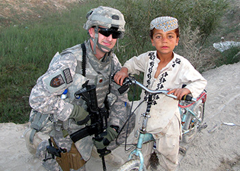 Army veteran James Seddon (UC San Diego) poses with a child on one of his tours in Afghanistan