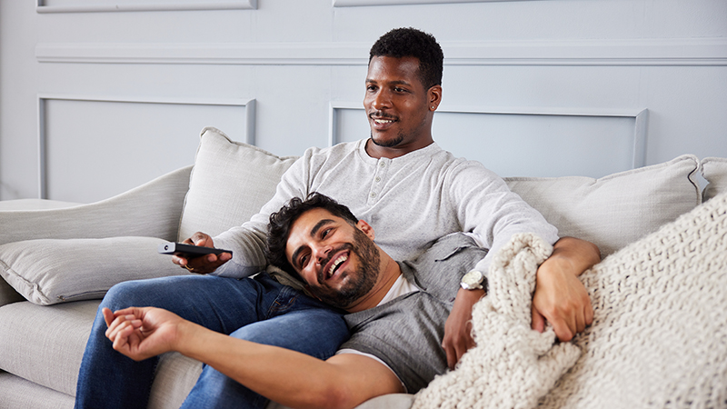 Young male couple watching tv while relaxing on their sofa