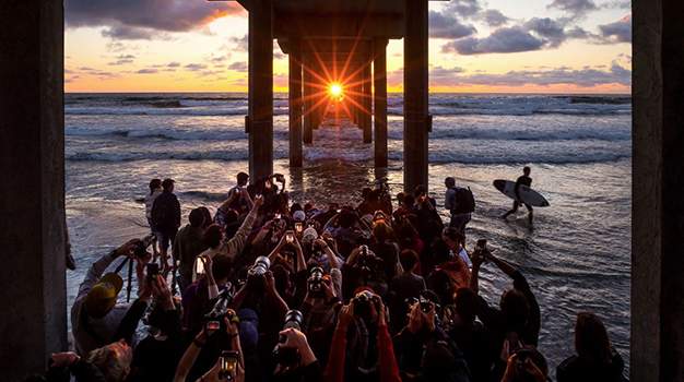 People photographing surfers at sunset