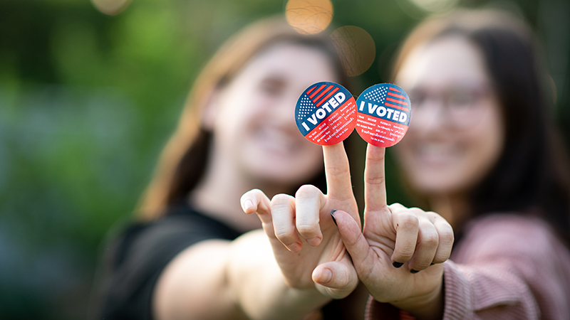 Portrait of two women holding out their hands together with the I voted stickers attached to their fingers