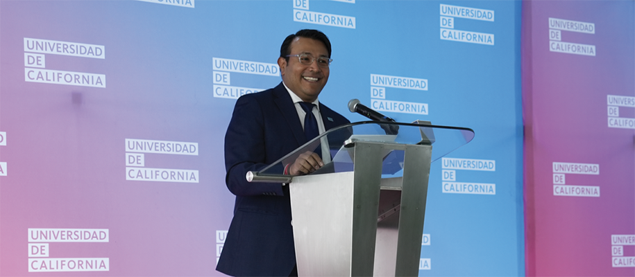 Jorge Silva speaks in front of a background filled with a Spanish-language version of the UC wordmark.