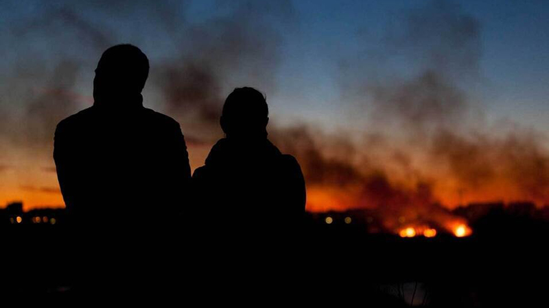 People holding hands at dusk overlooking wildfire