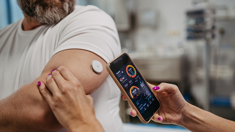 Doctor connecting patient's continuous glucose monitor with smartphone, to check his blood sugar level in real time. Obese, overweight man is at risk of developing type 2 diabetes. Concept of health risks of overwight and obesity.