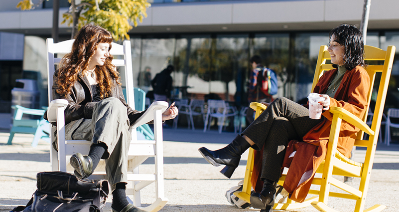 People talking while sitting in large rocking chairs outdoors