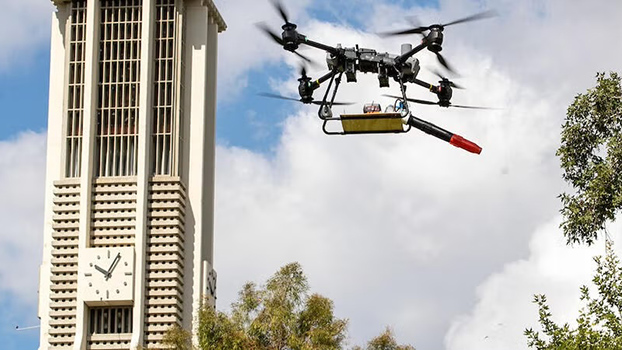 A leaf blower suspended in the air by a drone at UC Riverside