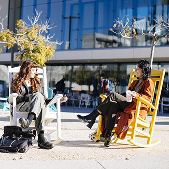 People talking while sitting in large rocking chairs outdoors