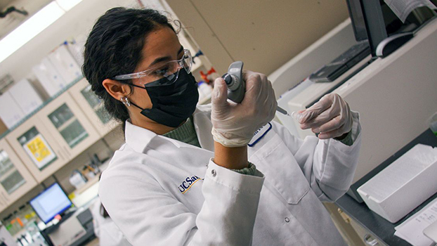 A white-lab-coat wearing student works in a lab