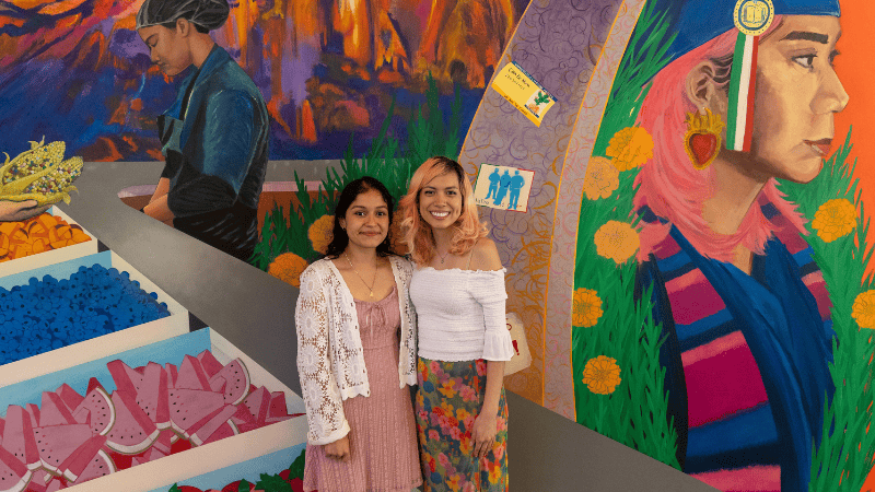 Two young women standing in front of a colorful wall