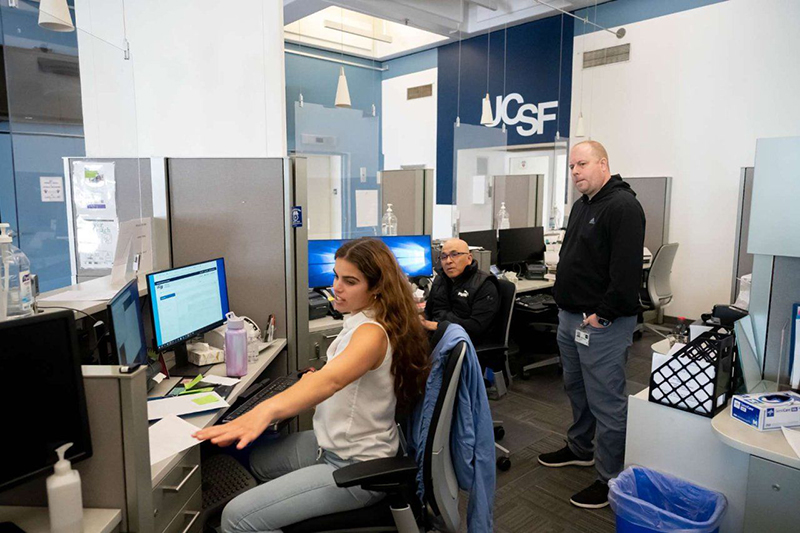David chats with colleagues sitting at their computer workstations