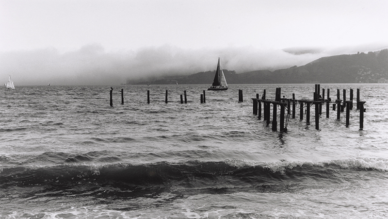 A view of the San Francisco Bay from Angel Island includes a sailboat just beyond the remains of a pier.