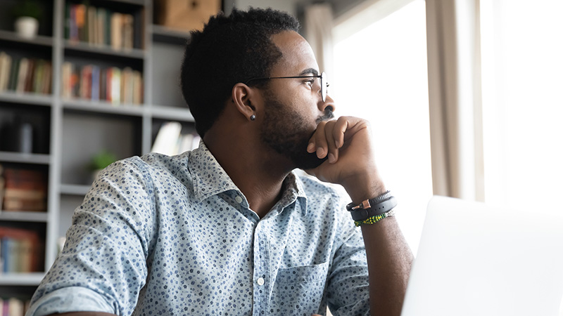 Thoughtful serious african professional business man sit with laptop thinking of difficult project challenge looking for problem solution searching creative ideas lost in thoughts at home office desk