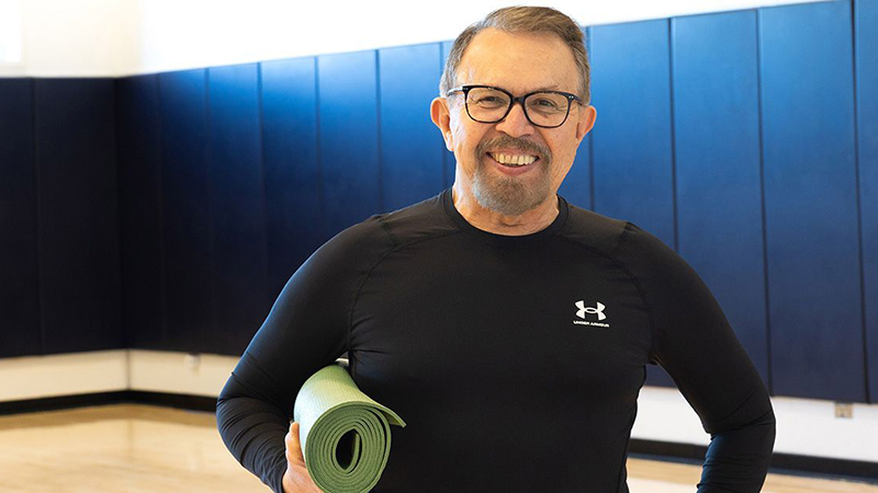 Smiling, Arturo holds a yoga mat