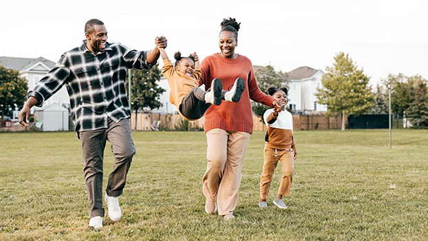 Family running across a lawn, swinging a child