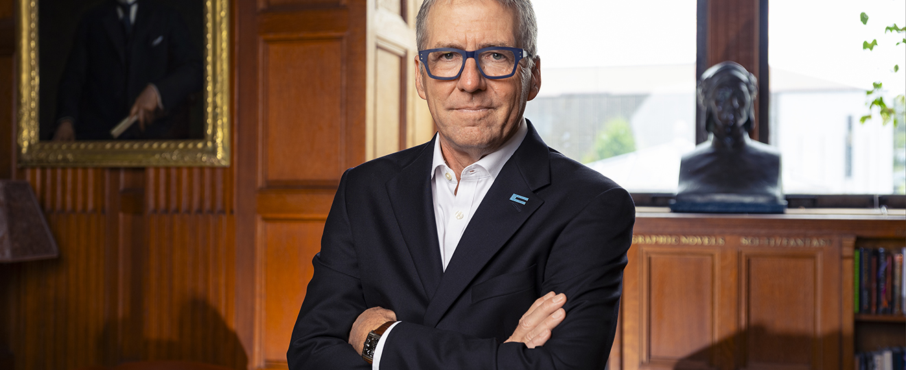 UC President James B. Milliken in a wood-paneled room wearing a suit