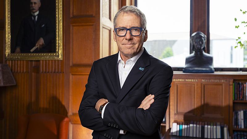 UC President James B. Milliken in a wood-paneled room wearing a suit