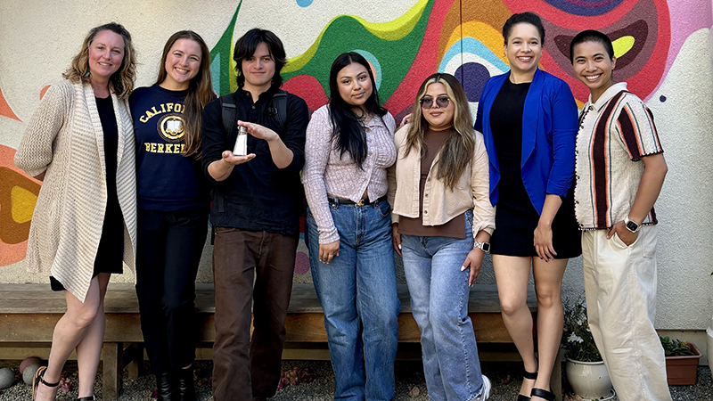 Group of people smiling and standing against a mural