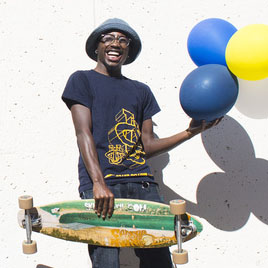 Man holding a skateboard and some balloons