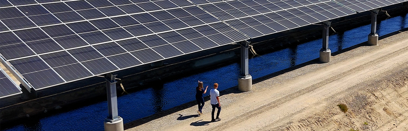 Two people walking along a canal covered with solar panels