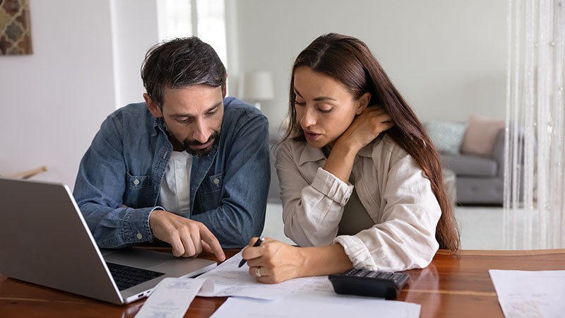 Middle aged couple discussing expenses at table with a laptop and calculator