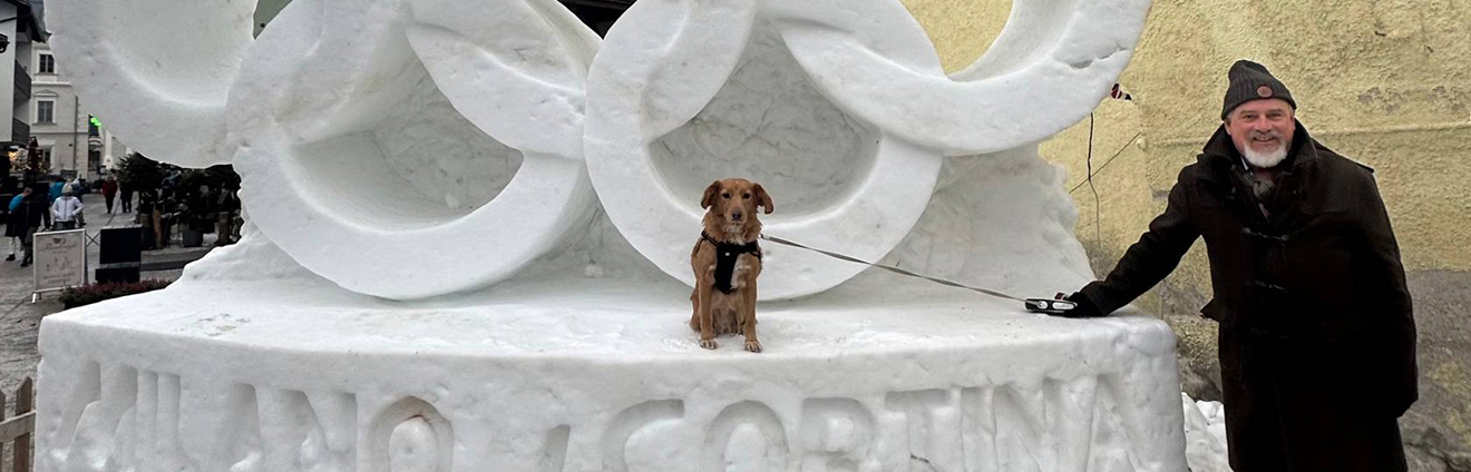 A man and his small dog next to an ice sculpture of the Olympic rings
