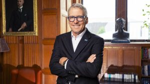 Pres. Milliken in a suit leaning against a desk