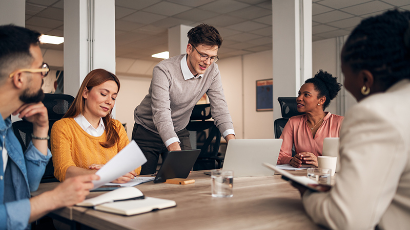A group of colleagues cooperating and brainstorming around a table in a contemporary professional office environment.