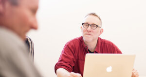 person with glasses and gray hair with a laptop in a meeting