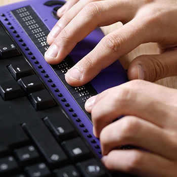 Visually impaired person using computer with braille computer display and keyboard.