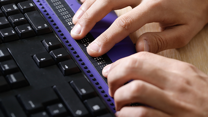 Visually impaired person using computer with braille computer display and keyboard.