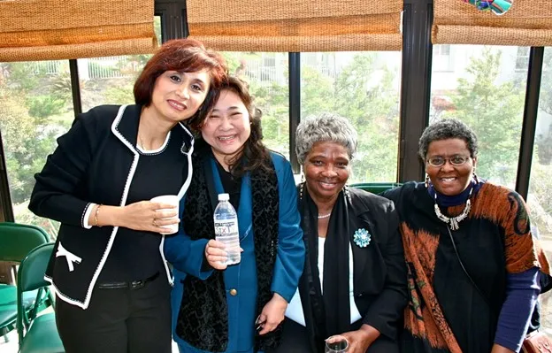Group of four smiling women standing together on a porch