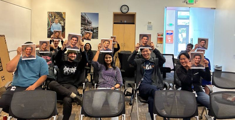 People sitting in a conference room holding up photos of Yash's face