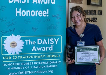 Nurse holding certificate, standing near colorful sign