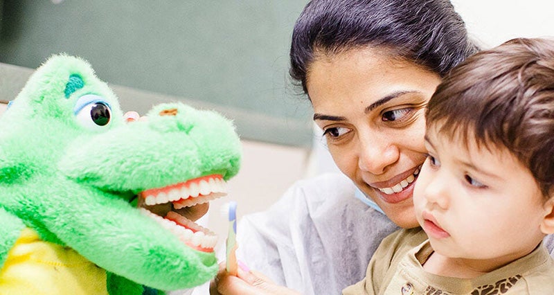 Dentist brushing a toy's teeth as child watches