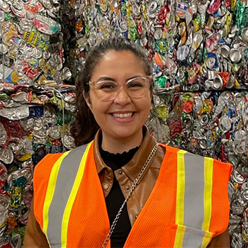 Woman in an orange safety vest standing in front of a wall of crushed metal cans