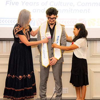 Two woman putting a sash around a young man