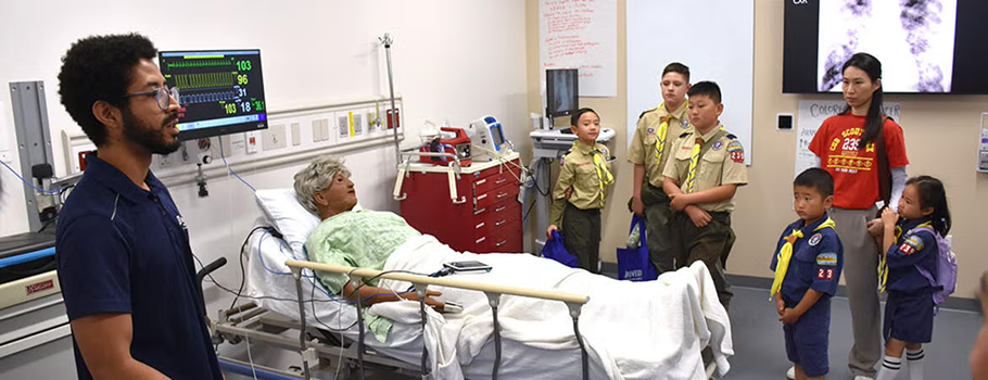Group of people standing around hospital bed with dummy patient