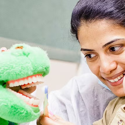 Dentist brushing a toy's teeth as child watches