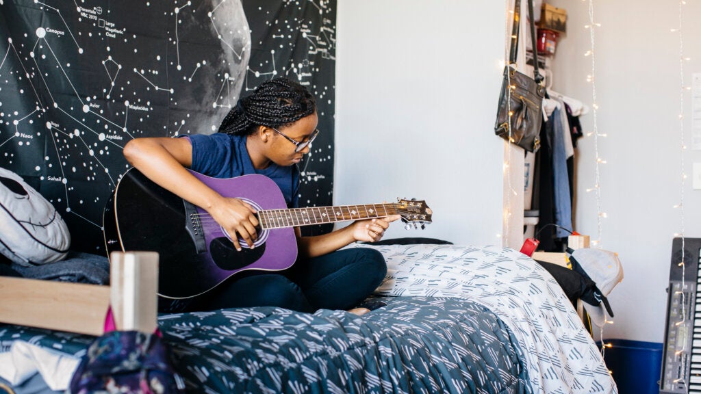 UC Merced student playing a guitar on her bed in a dormitory