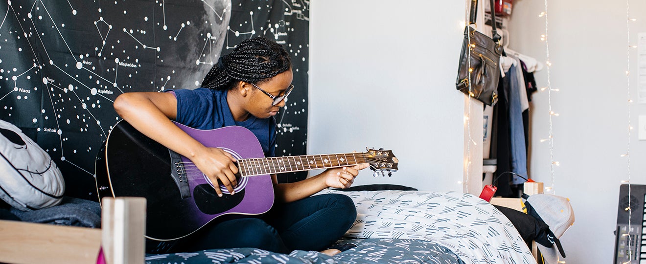 UC Merced student playing a guitar on her bed in a dormitory
