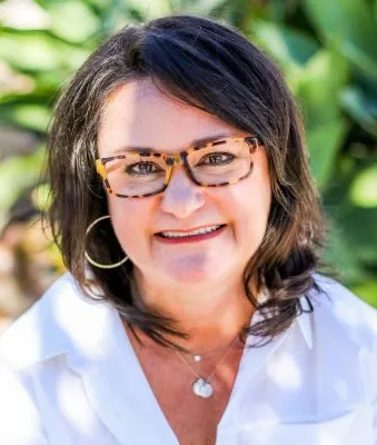 Alison Wolf headshot outdoors in white shirt and tortiseshell glasses