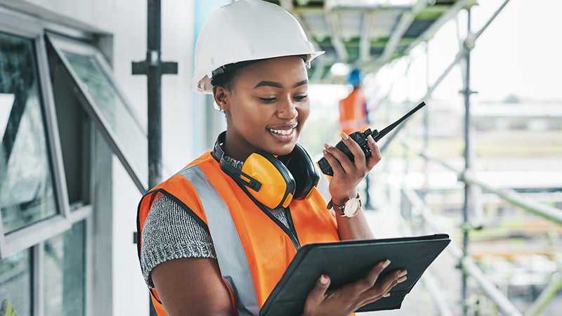 Tablet, engineer and black woman worker planning on a construction site strategy and talking on a walkie talkie. Project management, infrastructure and female contractor doing building assessment.