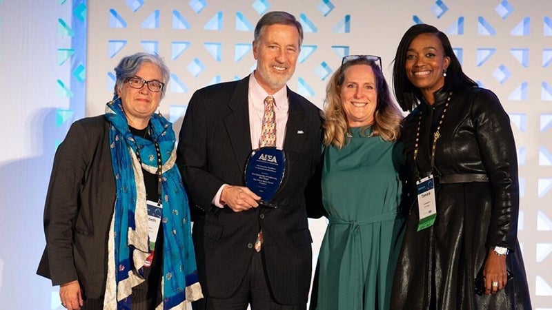 Four smiling people standing together and holding an award