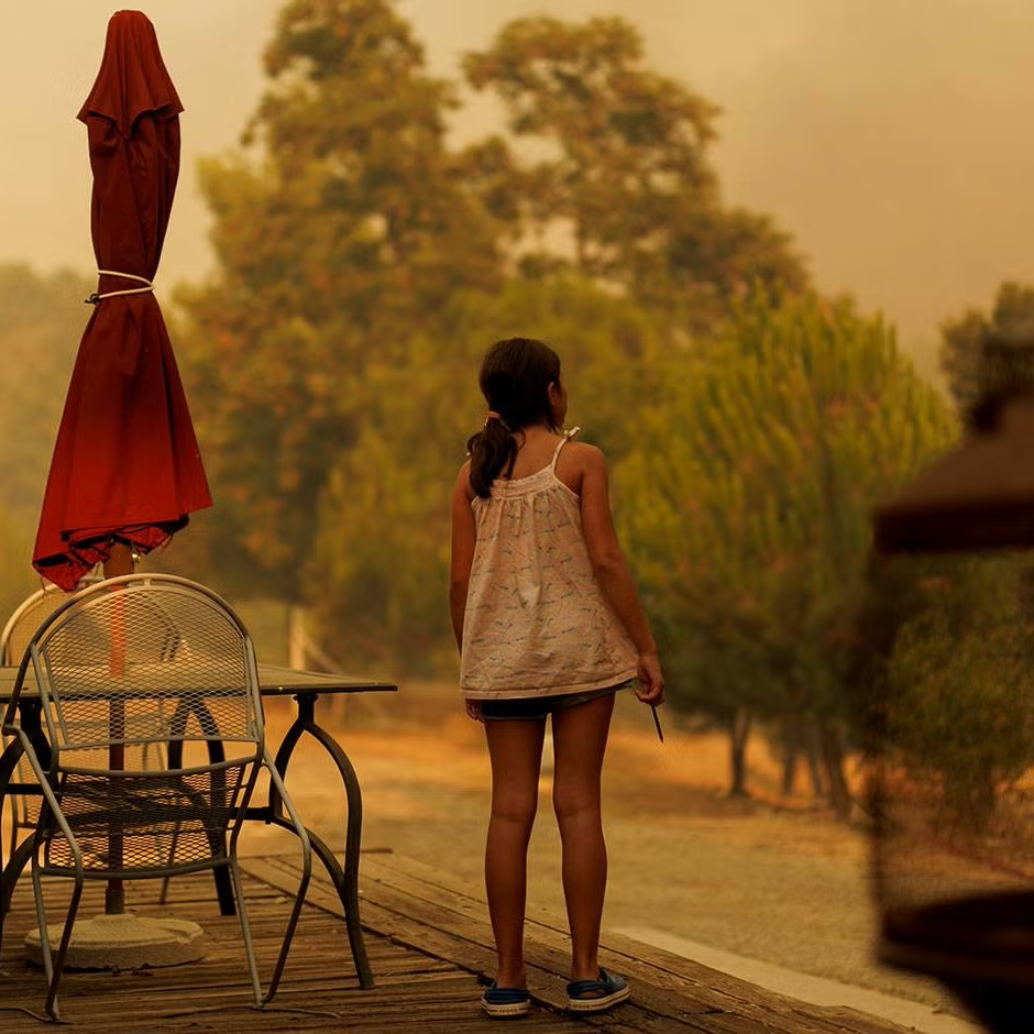 Young girl standing in front of house against a wildfire-induced orange smoky sky