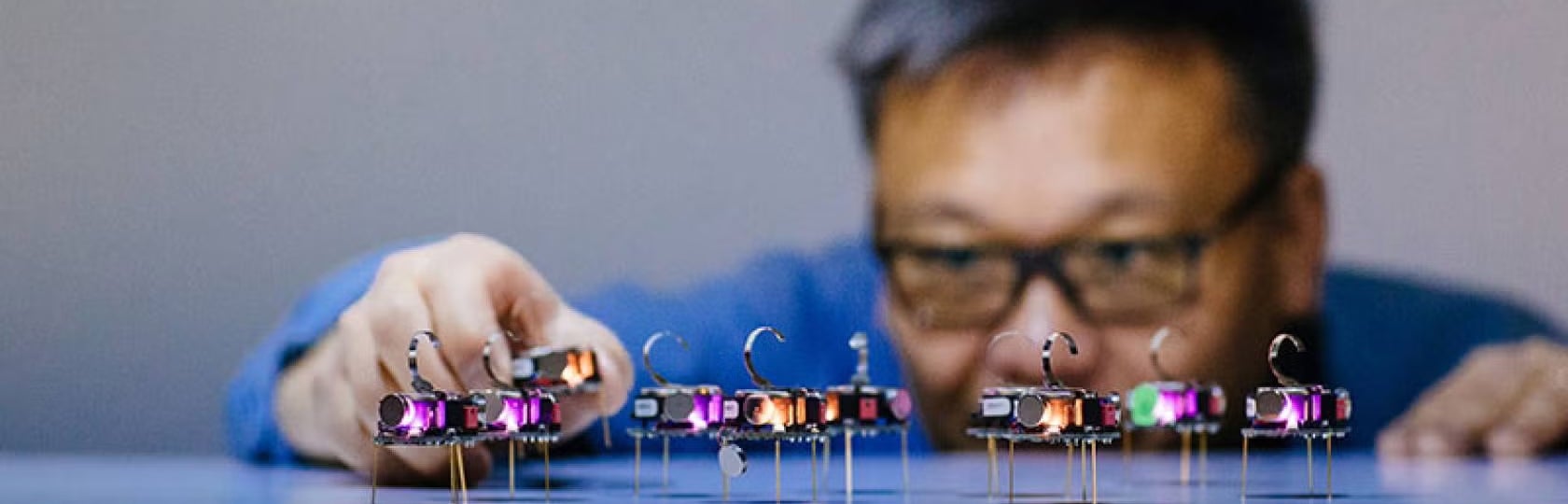 A researcher adjusts a row of small illuminated electronic devices on a reflective surface.