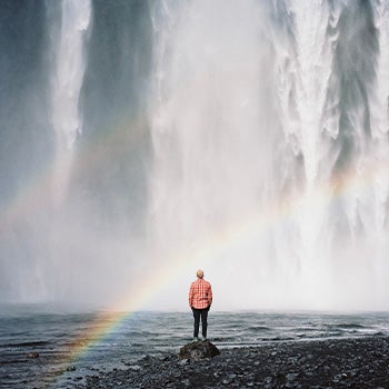 Person standing underneath a rainbow and in front of a waterfall