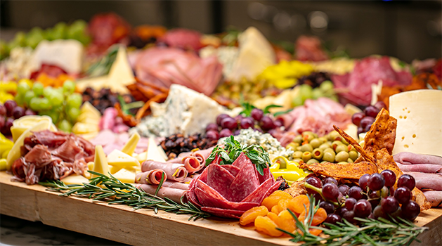 A charcuterie board with assorted meats, cheeses, grapes, olives and dried fruit.